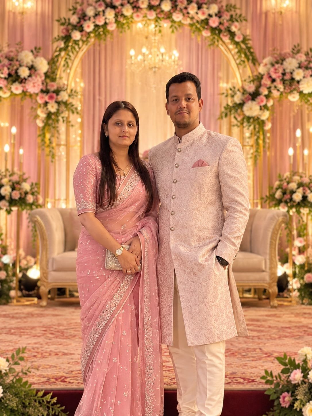 Riya and Ranjan standing together in front of a floral arch
